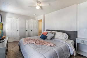 Carpeted bedroom with a textured ceiling, multiple closets, and a ceiling fan