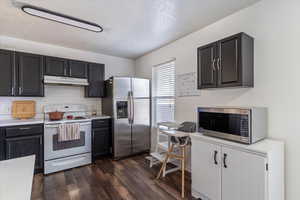 Kitchen featuring appliances with stainless steel finishes, backsplash, a textured ceiling, light countertops, and dark wood finished floors