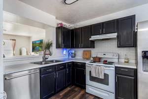 Kitchen featuring stainless steel appliances, a textured ceiling, light countertops, dark wood-style floors, and dark cabinets
