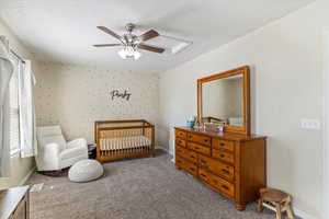 Carpeted bedroom with a nursery area, a textured ceiling, ceiling fan, and wallpapered walls