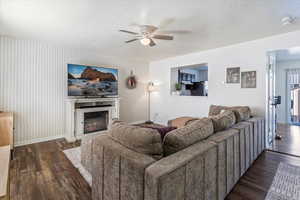 Living area with a textured ceiling, dark wood finished floors, ceiling fan, a glass covered fireplace, and an accent wall