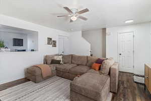 Living room with a textured ceiling, dark wood-style flooring, and a ceiling fan