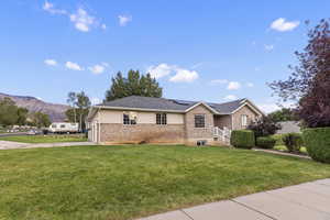 Ranch-style home featuring roof mounted solar panels, brick siding, a front yard, and a mountain view