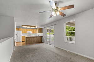 Kitchen with a textured ceiling, open floor plan, light countertops, white appliances, and light colored carpet