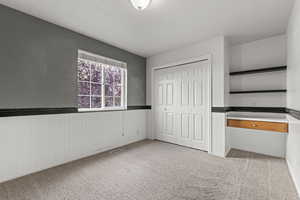 Unfurnished bedroom featuring light colored carpet, wainscoting, and a closet