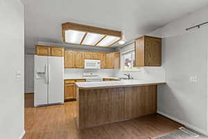 Kitchen featuring white appliances, light countertops, a peninsula, light wood finished floors, and brown cabinetry
