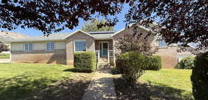 Ranch-style home with a front lawn, solar panels, and brick siding