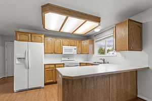 Kitchen featuring light countertops, white appliances, light wood finished floors, a peninsula, and brown cabinetry