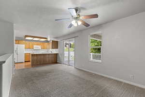 Kitchen featuring a peninsula, open floor plan, a textured ceiling, white appliances, and light carpet