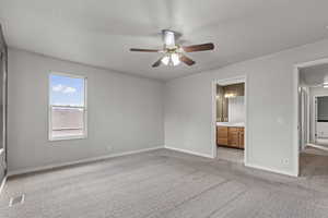 Unfurnished bedroom featuring light colored carpet, ensuite bath, and ceiling fan