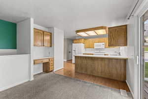 Kitchen with a peninsula, built in study area, white appliances, dark carpet, and light countertops