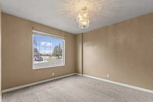 Carpeted spare room featuring baseboards and a chandelier