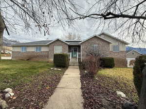 Single story home with a front lawn, roof mounted solar panels, and brick siding