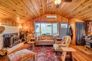 Living area featuring wood finished floors, wooden walls, lofted ceiling, a wood stove, and an AC wall unit