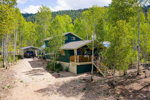 View of front facade with a porch, dirt driveway, a forest view, and a carport
