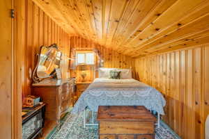 Bedroom featuring wooden walls, lofted ceiling, wood ceiling, and wood finished floors