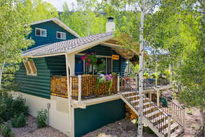 View of home's exterior with faux log siding, stairway, a chimney, a wooden deck, and a shingled roof
