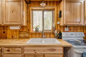 Kitchen featuring white range with electric stovetop, wooden walls, wooden counters, and light brown cabinetry