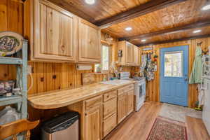 Kitchen featuring light wood-type flooring, white appliances, wood walls, light countertops, and a wood ceiling with exposed beams