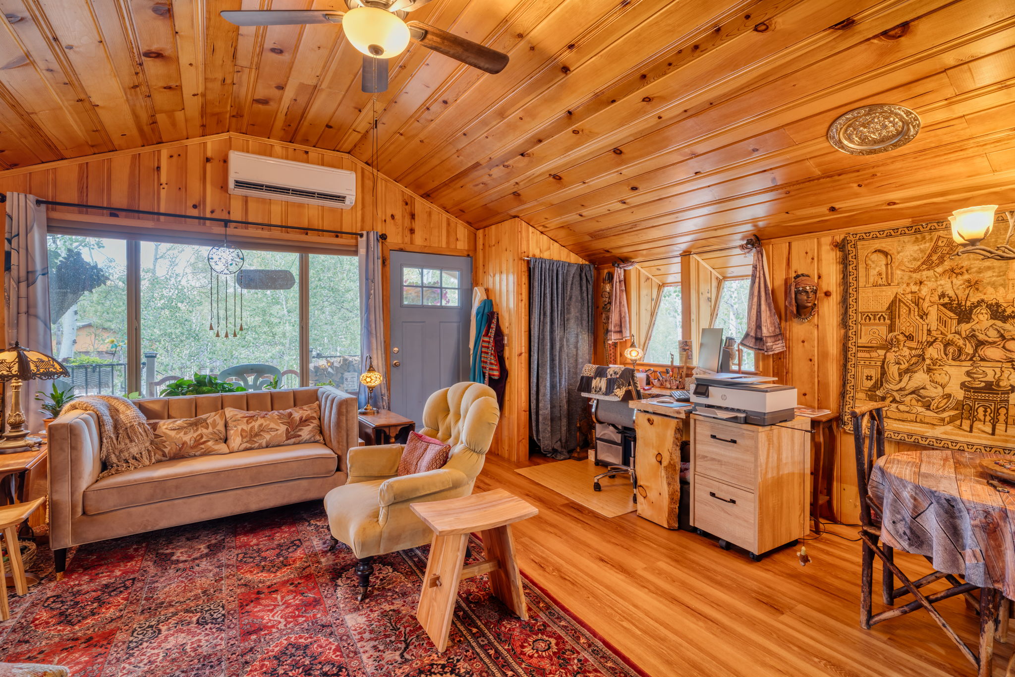 Living room with vaulted ceiling, wood walls, light wood-style floors, wooden ceiling, and a ceiling fan