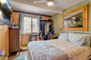 Bedroom with wooden walls, wood finished floors, ceiling fan, and a wood ceiling with exposed beams