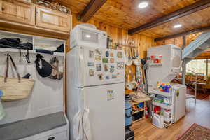 Kitchen featuring white appliances, wooden walls, light wood-style flooring, estacked washer and dryer, and a wooden ceiling with exposed beams