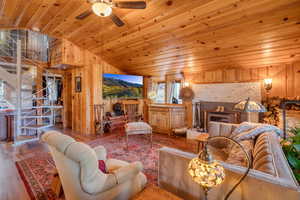 Living area with wood walls, wood finished floors, wood ceiling, vaulted ceiling, and a ceiling fan