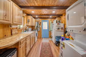 Kitchen with plenty of natural light, light wood-style floors, light countertops, white appliances, and a wooden ceiling with exposed beams