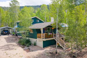 View of front of property featuring faux log siding, a detached carport, driveway, a forest view, and a chimney