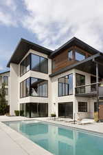Rear view of house featuring an outdoor pool, stucco siding, a balcony, and a patio