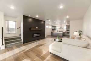 Living area featuring light wood-style flooring, stairs, a large fireplace, and recessed lighting