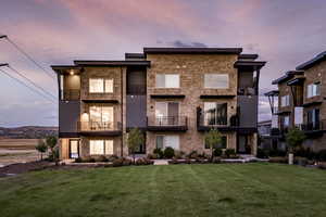Rear view of property featuring a balcony, a yard, and stone siding