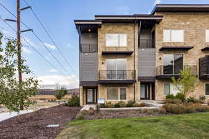 View of front of house featuring stone siding, a balcony, and a front yard