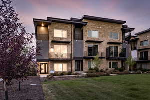 Contemporary home with a balcony, stone siding, and a lawn