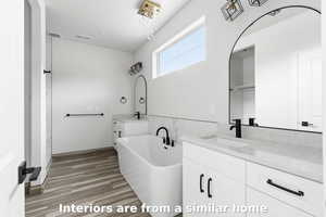Bathroom with two vanities, a soaking tub, and light wood finished floors