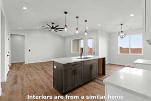 Kitchen with pendant lighting, light stone countertops, light wood-style floors, recessed lighting, and a center island with sink