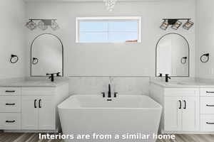 Bathroom featuring a freestanding tub, two vanities, wood finished floors, and tile walls