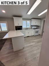 Kitchen featuring white cabinetry, decorative backsplash, white appliances, a peninsula, and light wood-style LVP floors