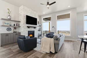 STAGED_Living area featuring light wood-style floors, ceiling fan, a stone fireplace, and built in features