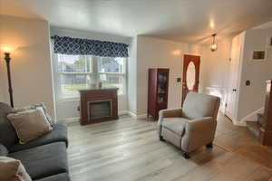 Living room with a textured ceiling, wood finished floors, a glass covered fireplace, and stairway