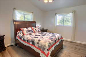 Bedroom with multiple windows, lofted ceiling, light wood-style flooring, and a ceiling fan