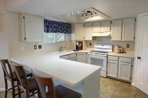 Kitchen featuring white electric stove, a kitchen breakfast bar, white cabinets, a peninsula, and light countertops