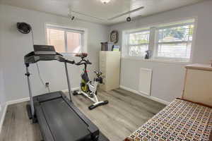 Workout area with rail lighting, a textured ceiling, and light wood finished floors