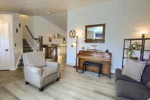 Living area with light wood-style flooring, stairs, and vaulted ceiling