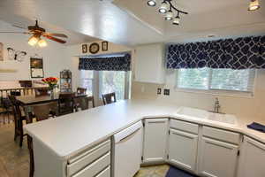 Kitchen with light countertops, white dishwasher, white cabinetry, a peninsula, and a ceiling fan