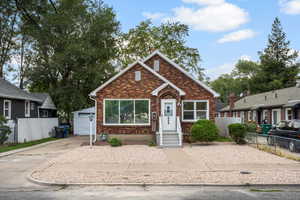 Bungalow with brick siding, an outbuilding, and a garage