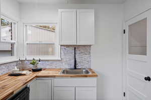 Kitchen with backsplash, wood counters, white cabinets, and dishwasher