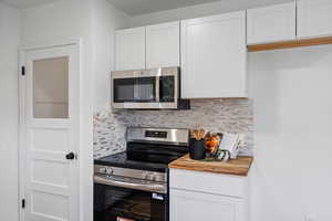 Kitchen with stainless steel appliances, white cabinetry, tasteful backsplash, and wooden counters