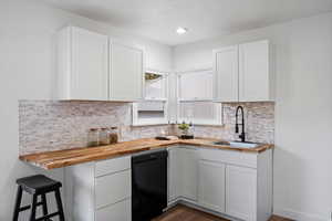 Kitchen with butcher block countertops, dishwasher, decorative backsplash, and white cabinets