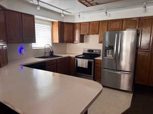 Kitchen with rail lighting, stainless steel appliances, light countertops, and a peninsula